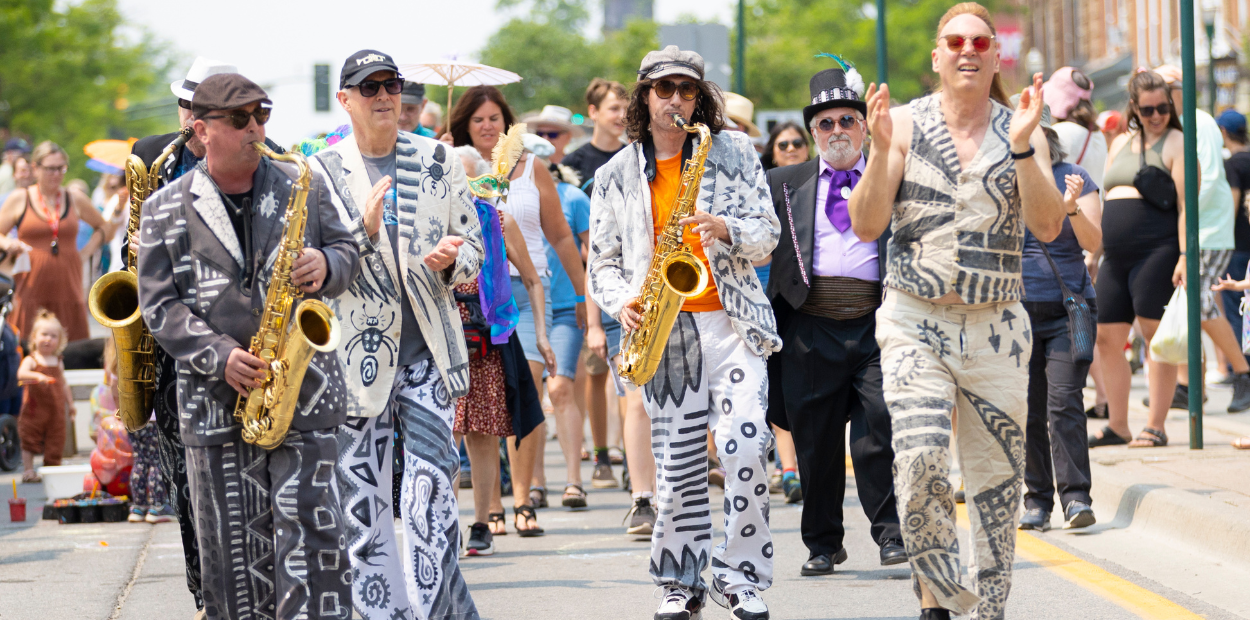 Two men with saxophones and two men clapping while marching in a parade.